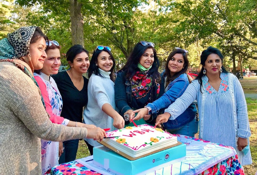 7 women outside surrounding a cake and smiling