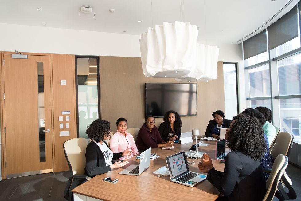 8 people sitting around a desk with laptops, talking