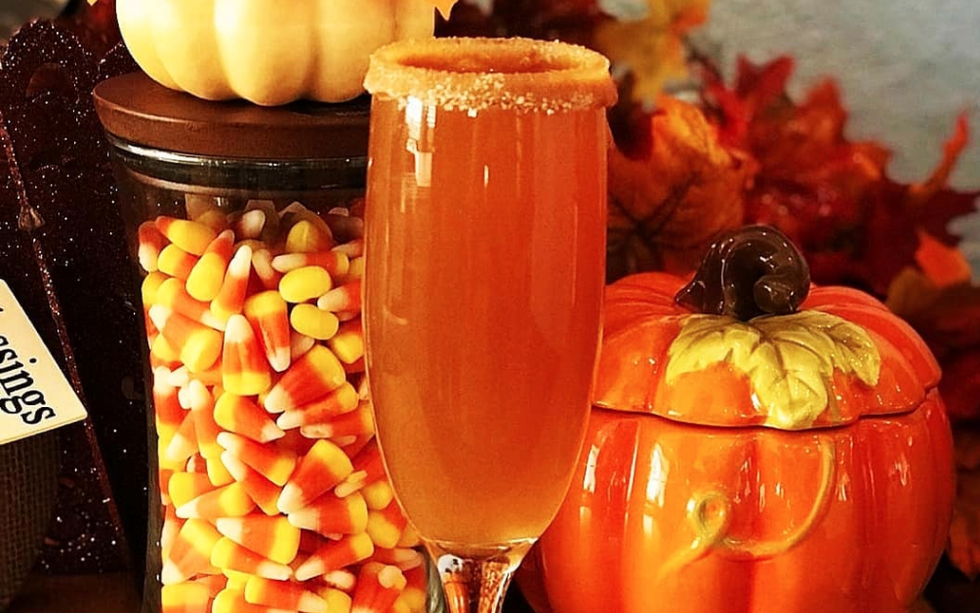 a champagne flute with an apple cider mimosa in it, a pumpkin-shaped jar behind it, and a jar of candy corn