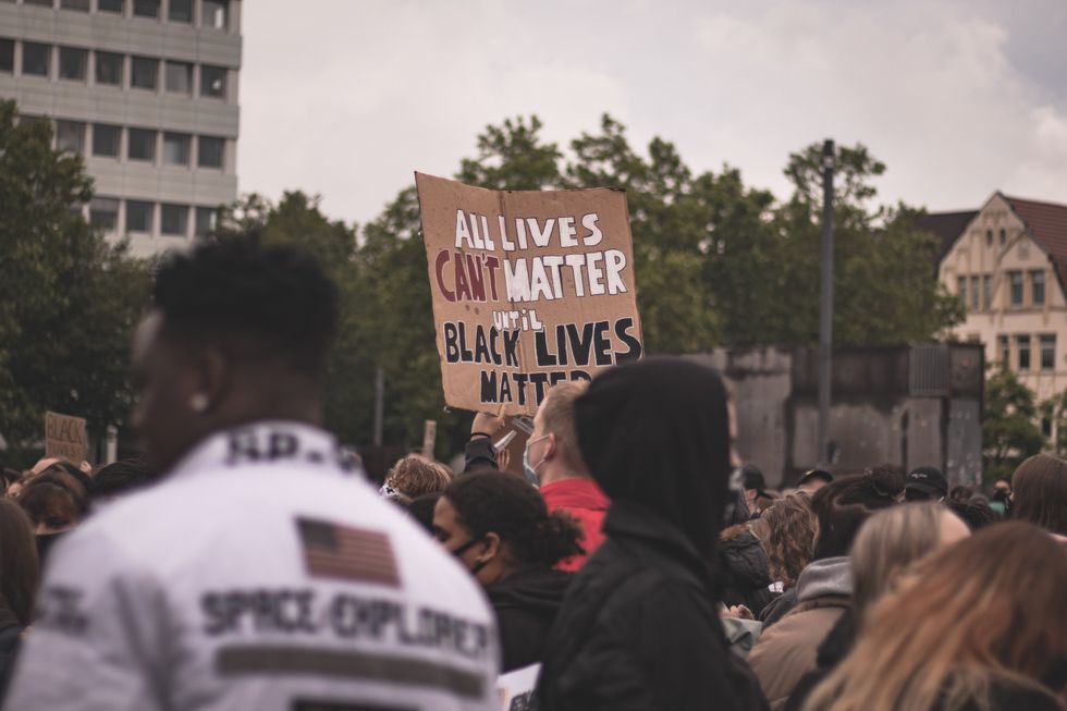 A crowd of people protesting one of them is holding a sign that says All Lives Can't Matter until Black Lives Matter