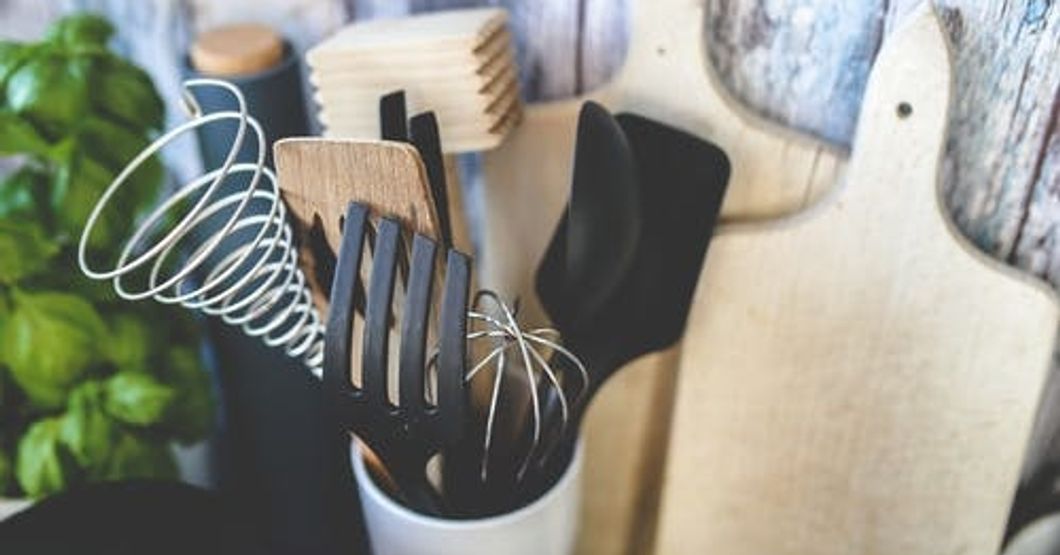 a cup filled with spatulas, whisks, and spoons, in front of a couple cutting boards.