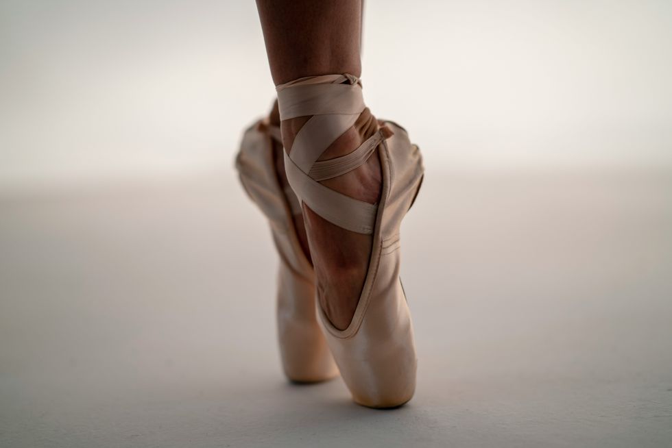 A dancer's feet en pointe in ballet shoes with ribbons against a soft background.