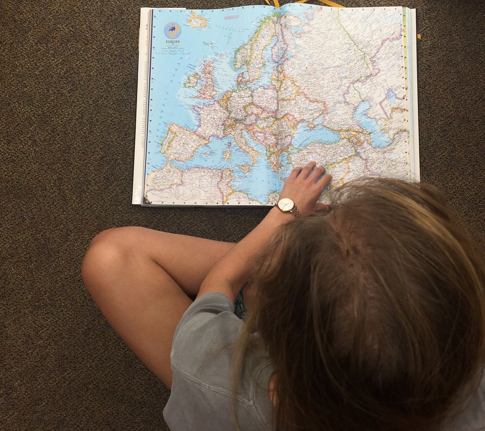 A girl is looking at a book of maps of the world. 