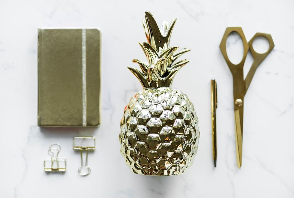 A golden pineapple decor next to scissors, pen, and a book on a marble surface.