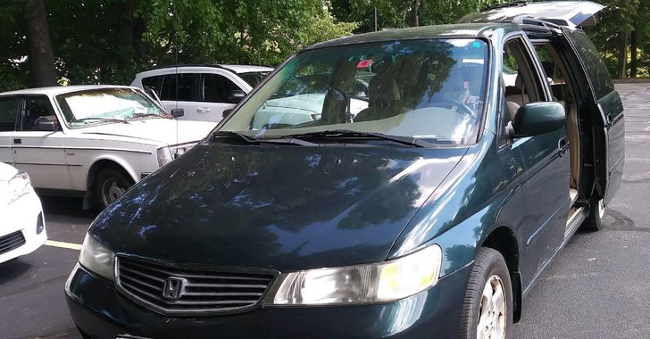 A Green Honda Odyssey van with its doors open parked in front of the white Volvo