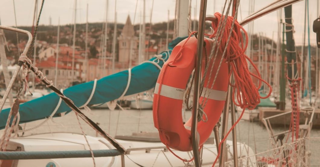 a life saver and rope attached to a boat in a marina full of boats.
