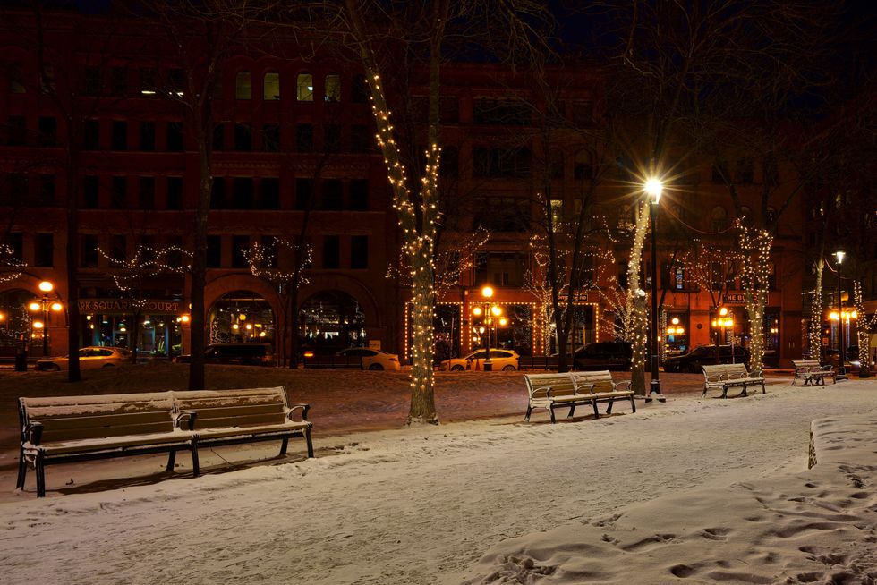 A lit street with snow on the sidewalk.