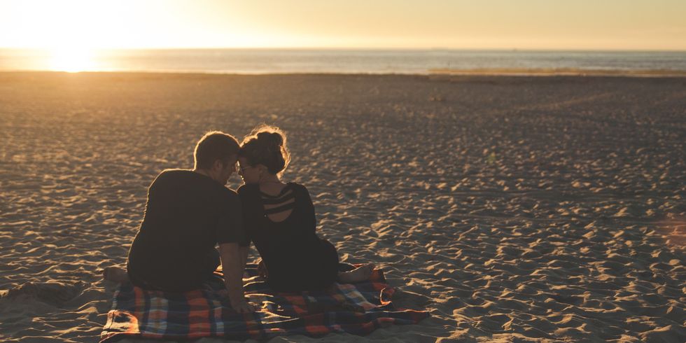 a man and a woman sitting on the beach in front of the sunset