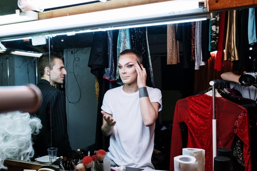 a man in a dressing room putting on drag makeup and looking fierce.