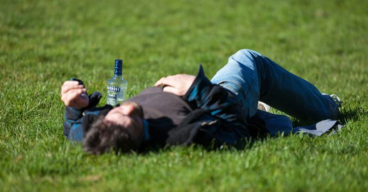 a man laying in the grass with a bottle of vodka