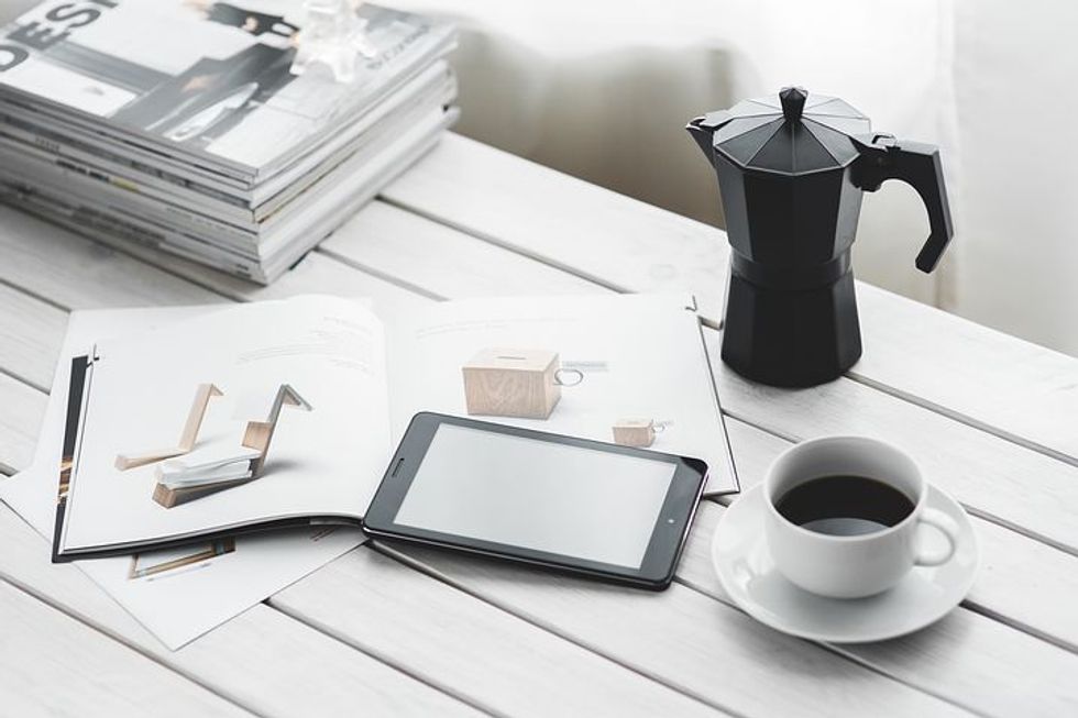 A modern workspace with a tablet, coffee, and magazines on a white table.