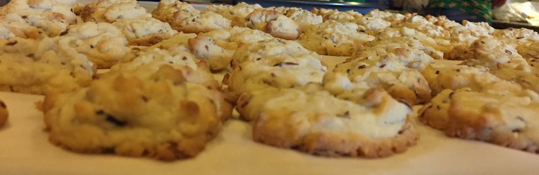 A photo of cookies cooling on top of parchment paper. They're almond-flavored cookies that are white and bumpy because of the almonds sticking out.