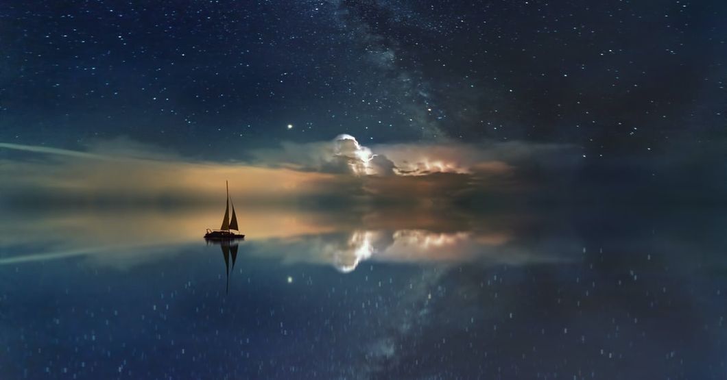 a sailboat on the water as it reflects the night sky and seems to become a void.