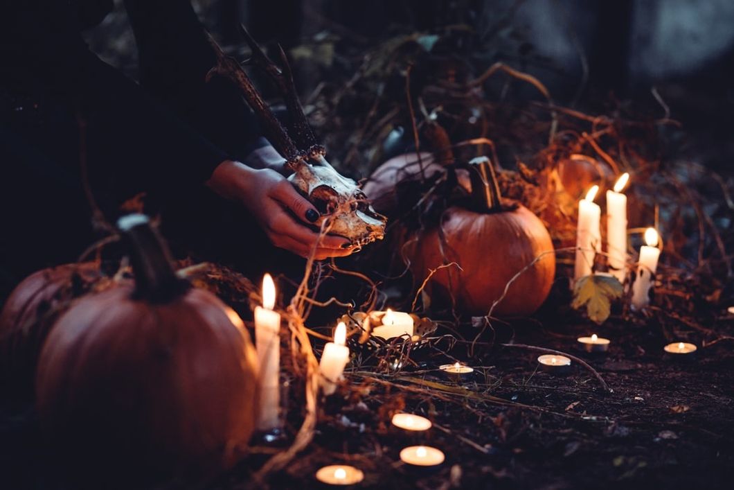 a scene of candles, pumpkins, and a pair of hands holding the skull of a horned animal.