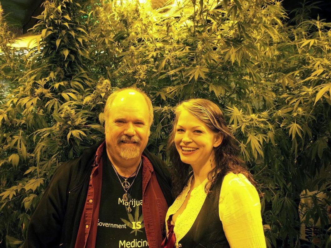 A smiling man and woman in front of a large cannabis bush