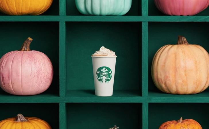 A starbucks cup on a shelf with whipped cream, surrounded by pumpkins