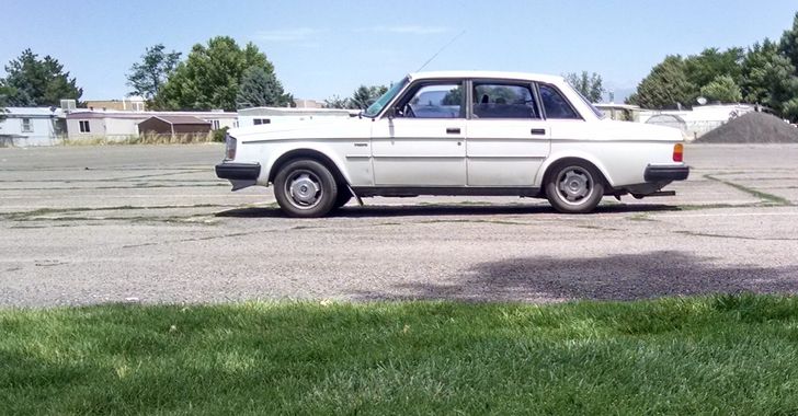 A white 1983 Volvo sedan sitting on concrete with grass in front of it
