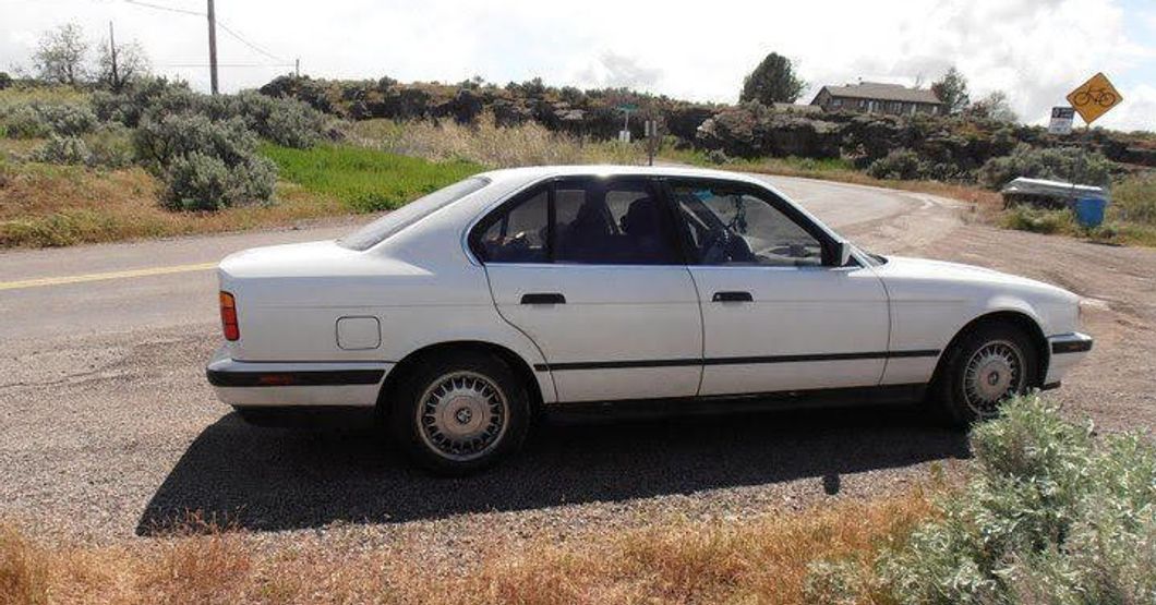 a white BMW 525 sitting on the side of a road with brown grass
