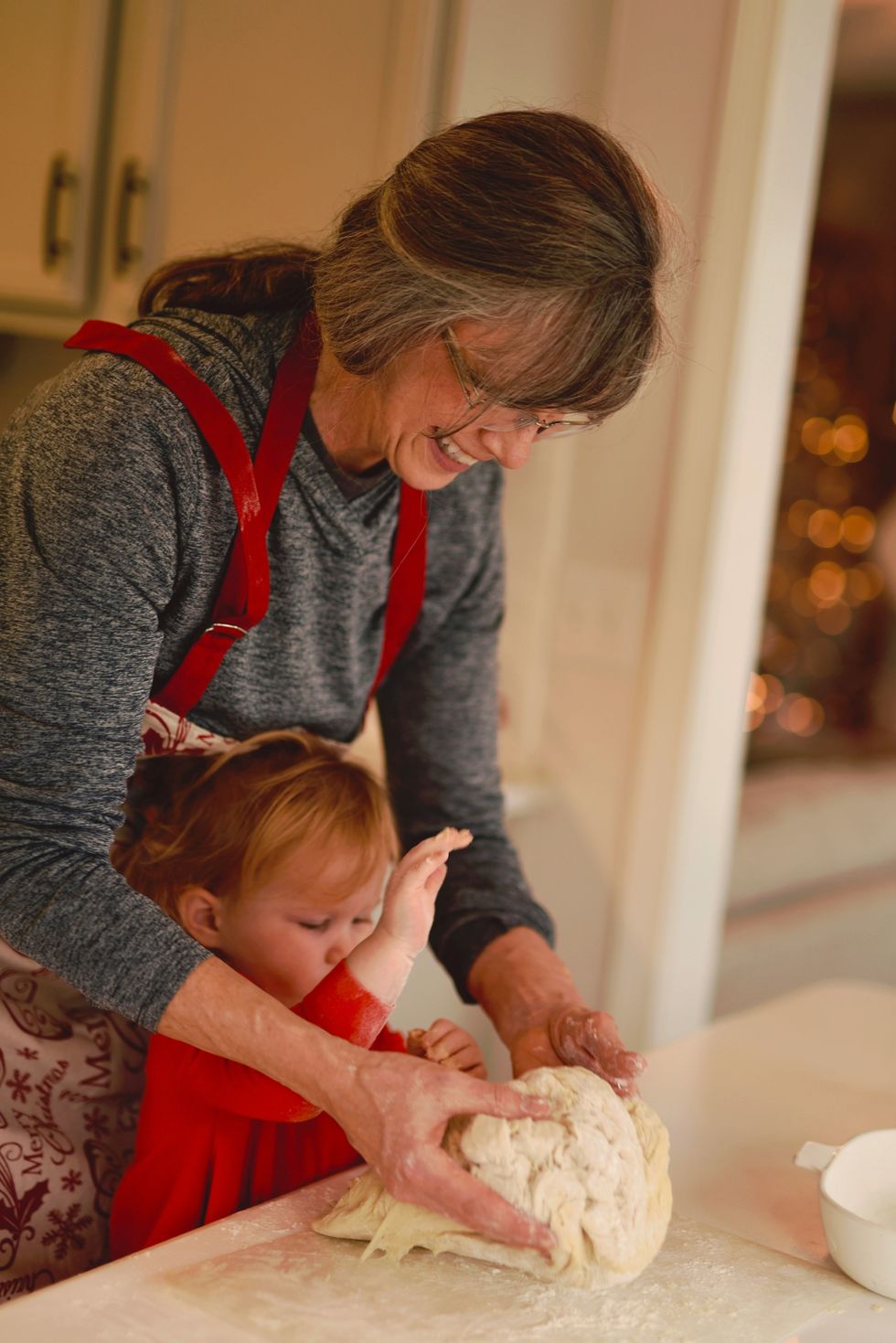 A women and toddler kneading dough together on a kitchen counter.