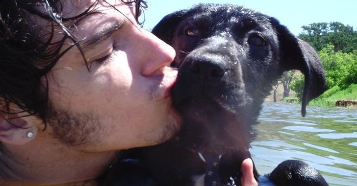 A young man holding a small black lab in the water