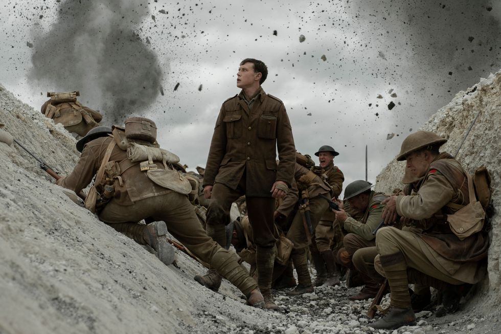 Actor George MacKay as Lance Corporal Schofield looks on at No Man's Land as bombs explode and scatter debris. Others soldiers cower in the trench of this World War One battlefield in the movie 1917.