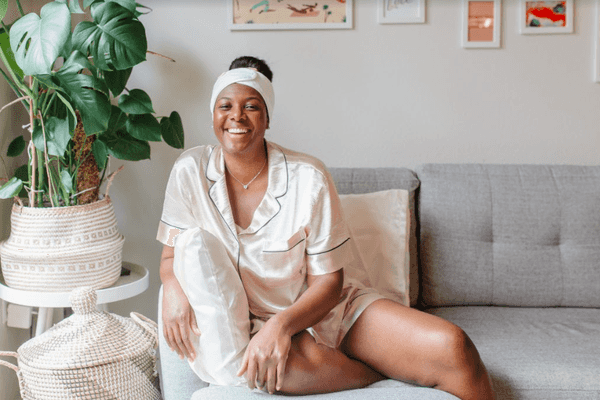 Alisia Ford smiling, sitting on couch wearing satin pajamas