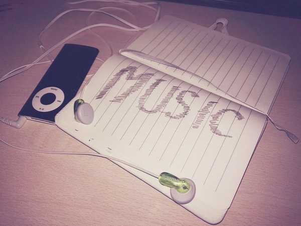 An open notebook with the word MUSIC scribbled in large letters, and an old iPod with a pair of earbuds sitting to the side.