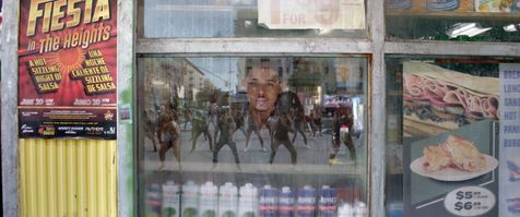 Anthony Ramos (as Usnavi) looks out his bodega's window at a street filled with people dancing in the streets of Washington Heights. You see the crow'd reflection in the window. The movie still is from Warner Brothers' "In The Heights."