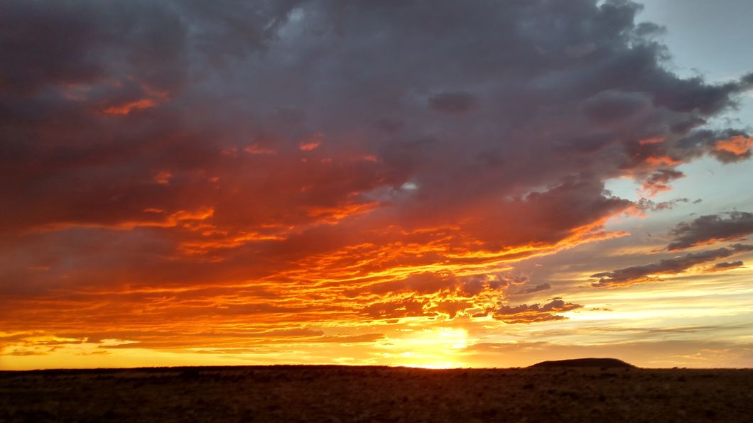 Bright red and orange sunset behind a hill and dark foreground