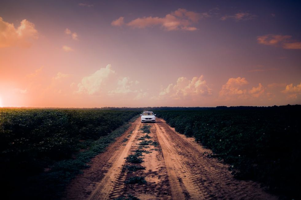 Car on a dirt road among fields at sunset.