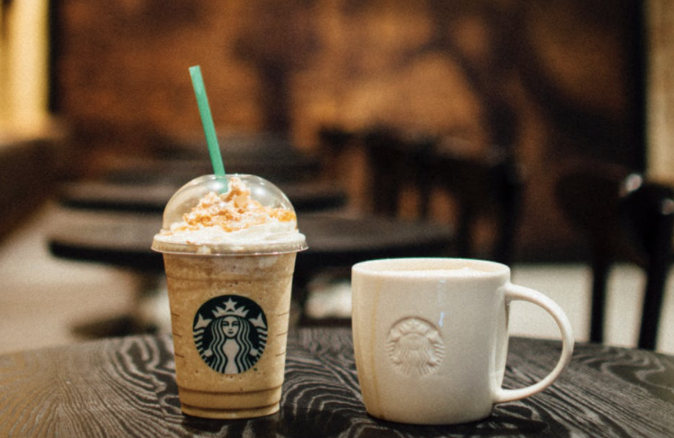 Caramel Frappuccino from Starbucks sitting beside white Starbucks coffee cup on a black wooden table.