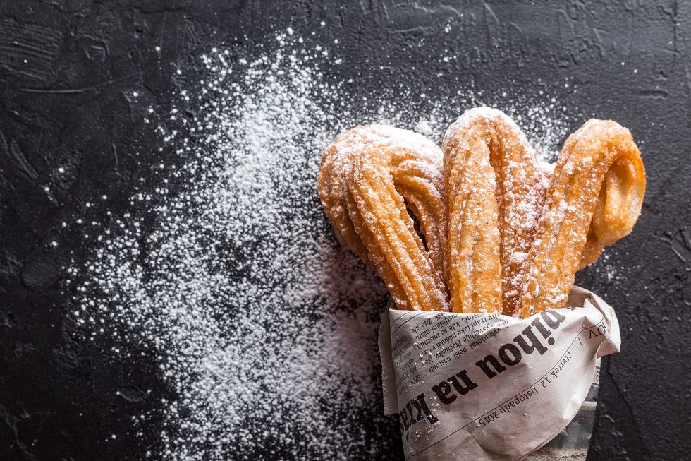 Churros, black table background, powdered sugar, newspaper used as holder for Churros