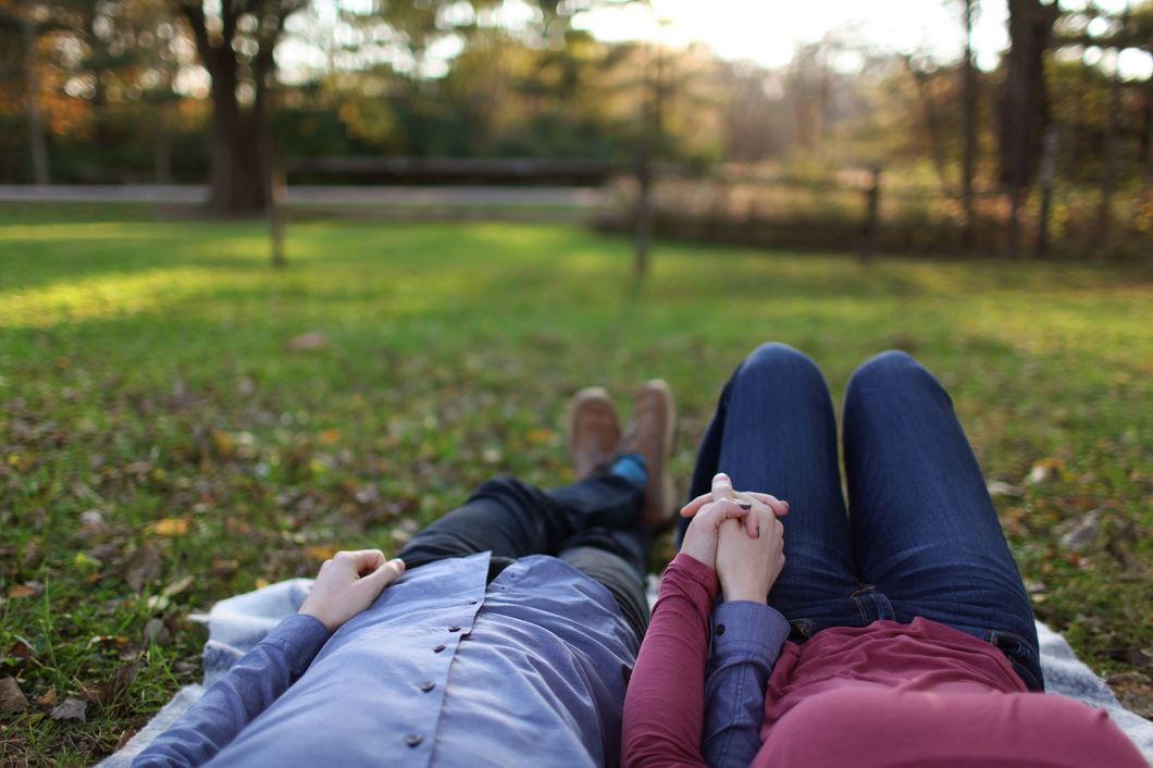 couple holding hands while lying in the park