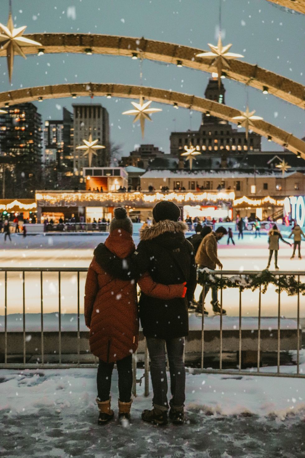 Couple standing in the snow watching ice skaters
