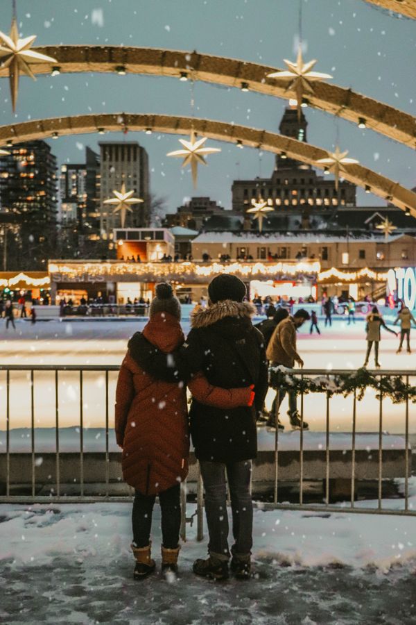 Couple standing in the snow watching ice skaters