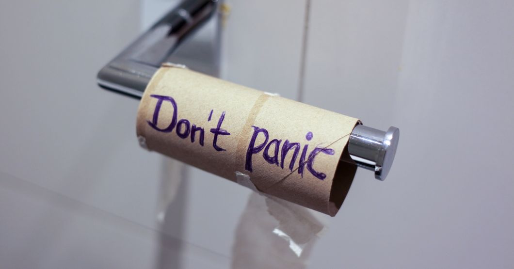 Empty toilet paper roll hanging in a toilet stall that says Donet Panic written on it. 