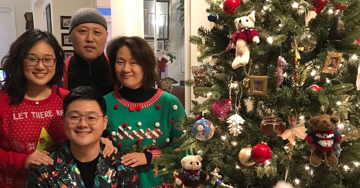 Family in festive sweaters posing by a decorated Christmas tree.