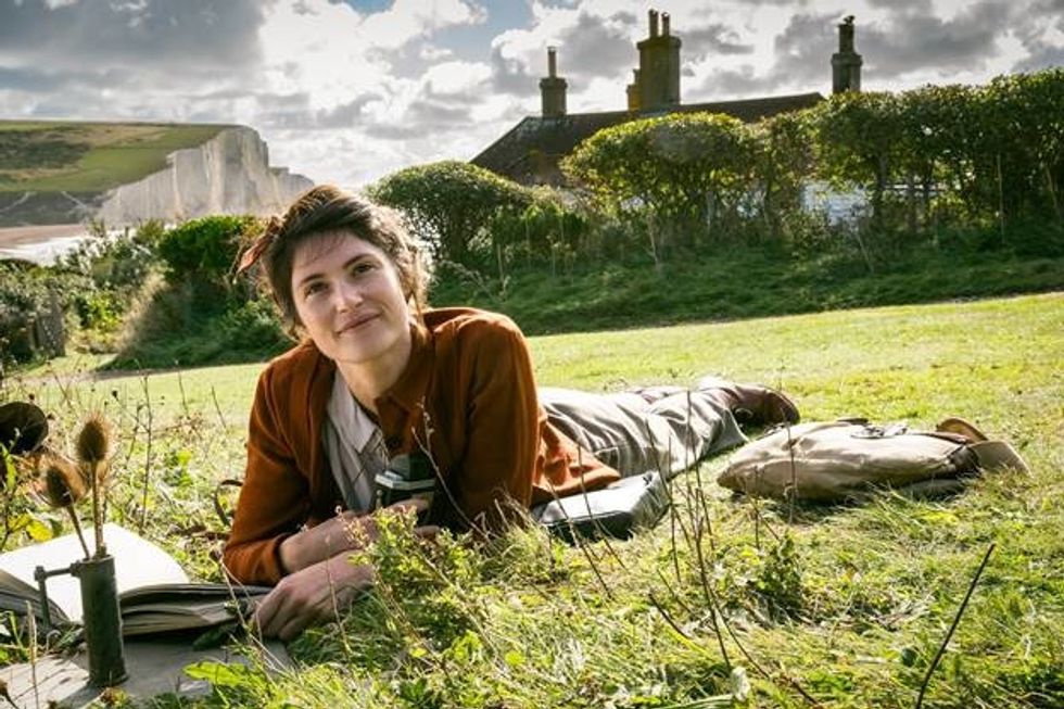  Gemma Arterton plays Alice, a reclusive writer in Southern England, in British World War II drama "Summerland." She is lying belly down on the grass atop a hill with a book in her hand. She is smiling as her gaze is looking up.