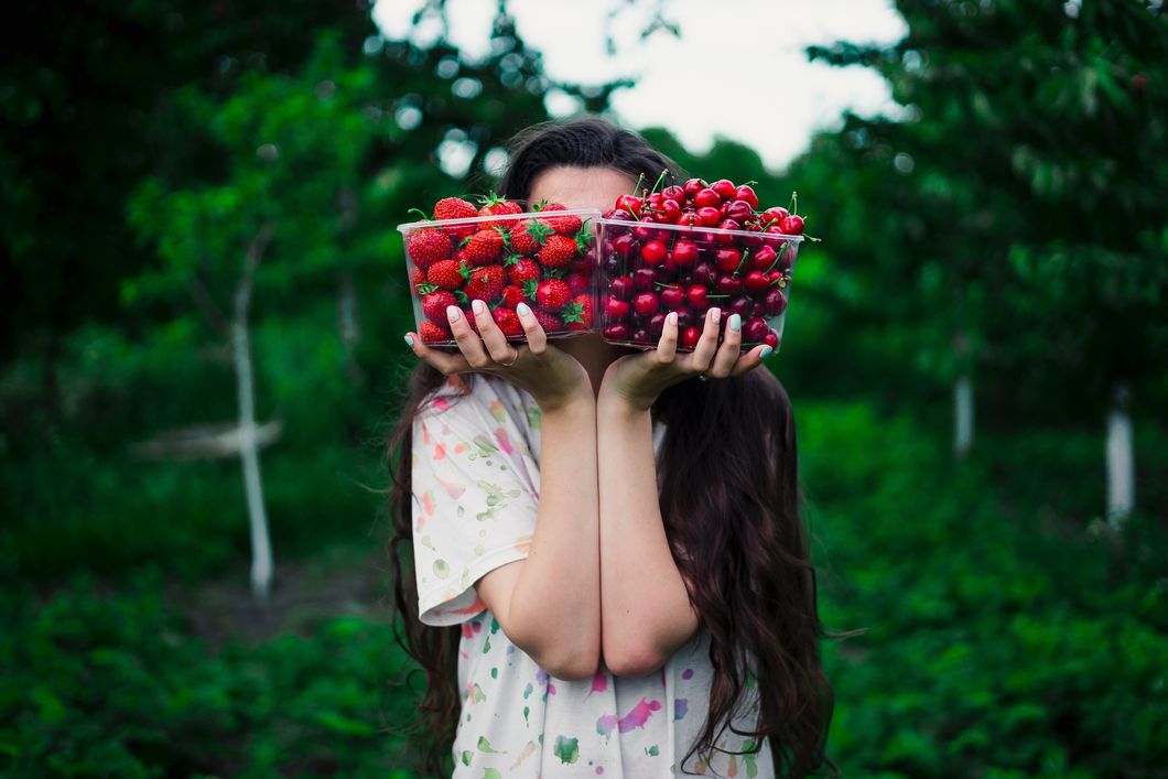 Girl covering face with strawberries and cherries.