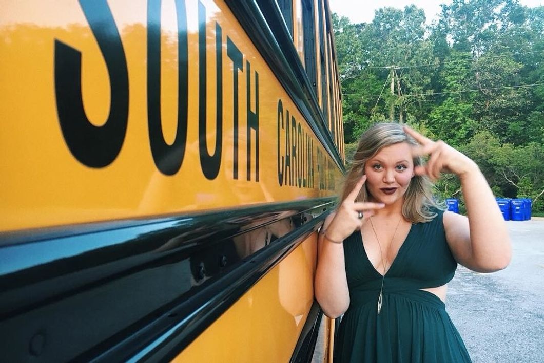 girl going to prom standing next to school bus