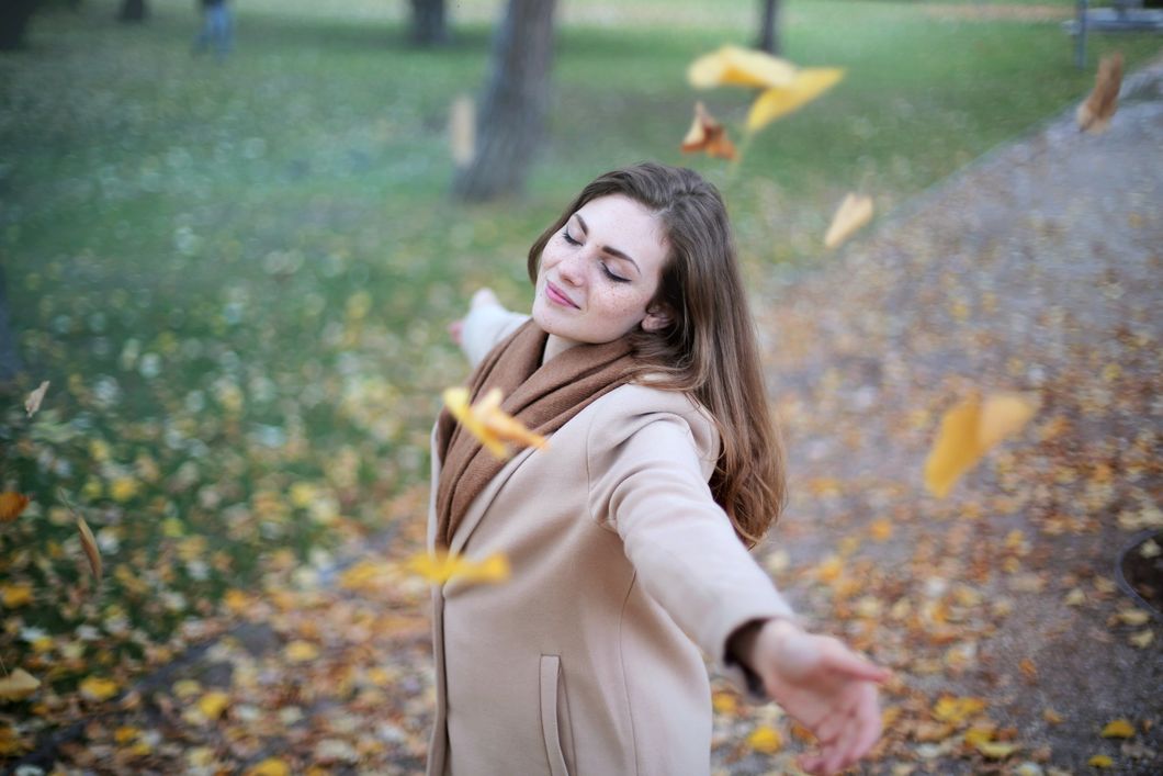 Girl holding her arms out as leaves fall down