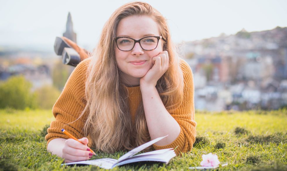 Girl in glasses holding a pencil to a notebook and looking as if she is in thought