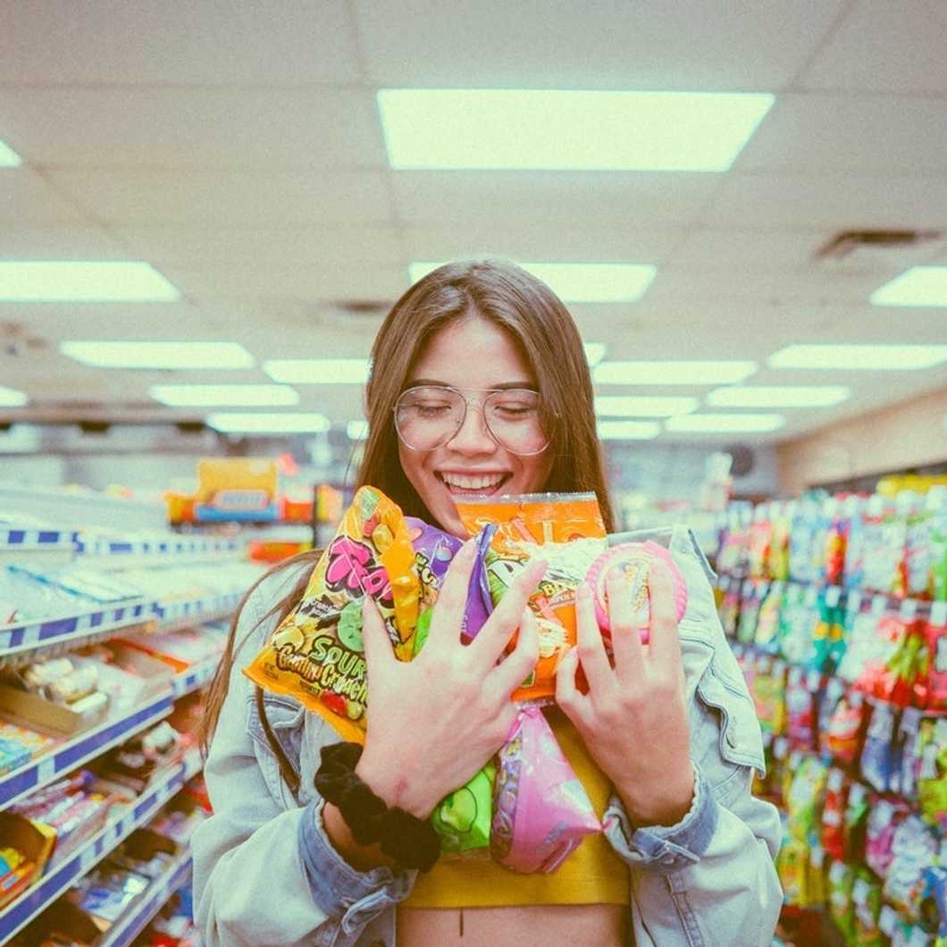 girl in grocery store holding armful of candy