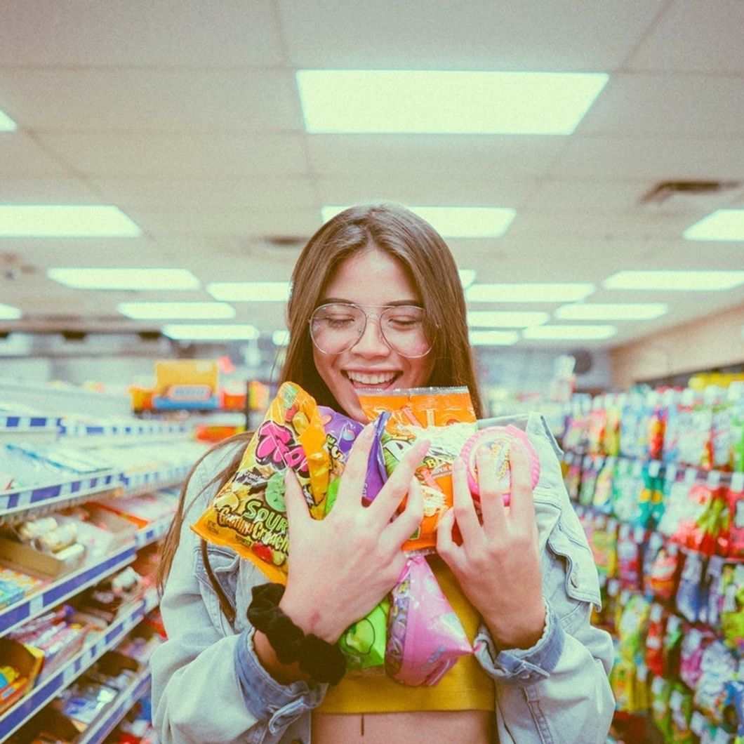 girl in grocery store holding armful of candy