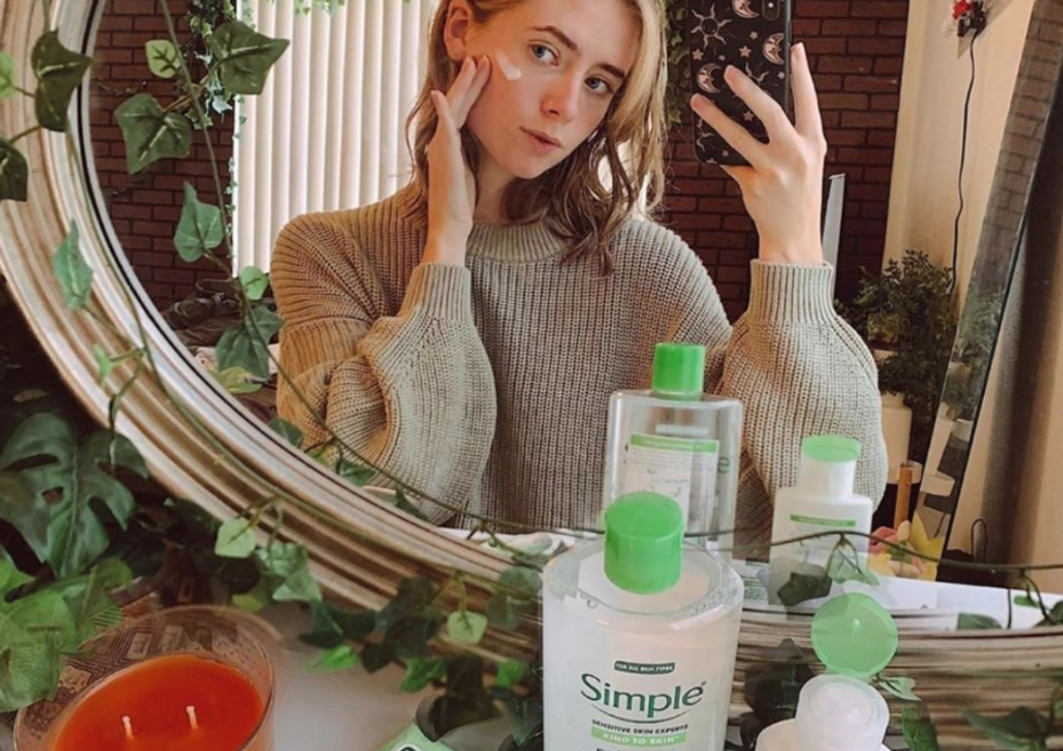 girl in sweater taking selfie while putting lotion on her face