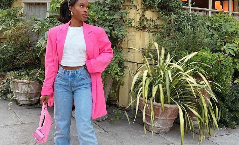 girl in white t-shirt, pink blazer, and baggy denim in front of lush, green plants