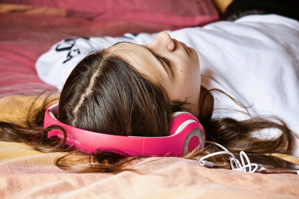 Girl laying on bed listening to music with headphones