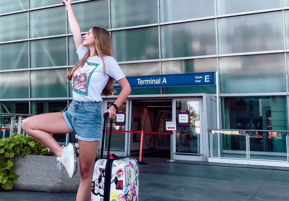 girl posing with suitcase outside in front of airport
