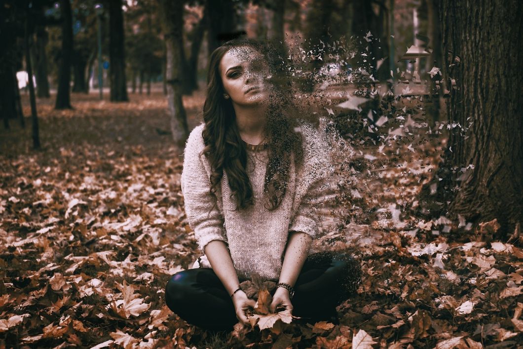 Girl sitting on ground with one half of her body disintegrating into the air.