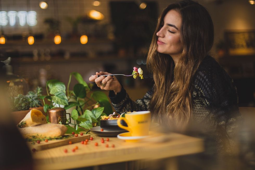 girl smiling and eating pasta at a table with green plants around her